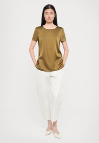 Satin olive green top with short sleeves and a rounded neckline, paired with loose white trousers and cream-colored pointed shoes.