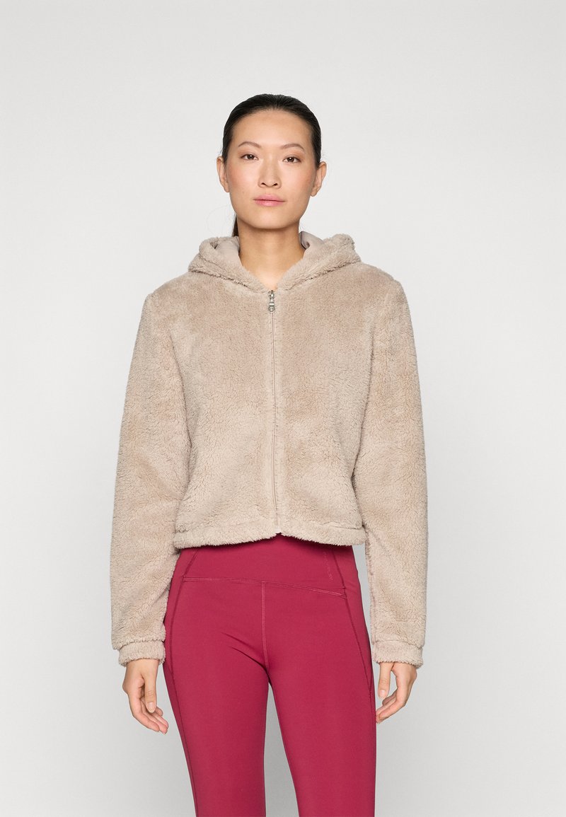 Haut à capuche beige flou avec fermeture éclair, au design court et texture douce. Assorti avec des leggings bordeaux taille haute.