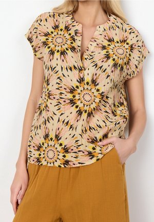Bluzka z krótkim rękawem z kołnierzykiem, w kwiatowy wzór w beżowym kolorze z żółtymi, różowymi i czarnymi motywami, zestawiona z luźnymi spodniami w kolorze musztardowym. Lekka tkanina.