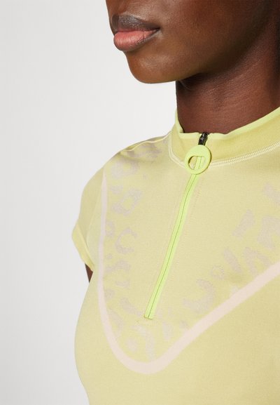 Haut de sport jaune à manches courtes avec une fermeture éclair sur le devant, présentant un motif texturé et un accent rose clair contrastant le long du col.
