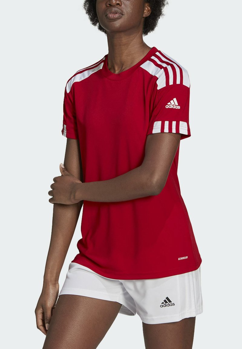 Rotes Sporttrikot mit weißen Streifen auf den Schultern, kurzen Ärmeln und schlanker Passform. Getragen mit weißen Shorts, die ein Adidas-Logo tragen.