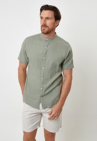 Kortærmet, lysegrøn skjorte med mandarin krave, knaplukning og blød tekstur, sammen med lyse shorts.