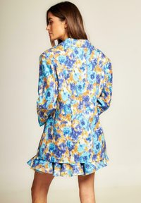 Blazer floreale in tonalità di blu, arancione e giallo, con tessuto testurizzato e una vestibilità rilassata, caratterizzato da maniche lunghe e un orlo arricciato.