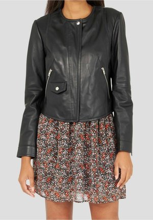 Mujer que lleva una chaqueta de cuero negra con bolsillos con cremallera sobre una falda con estampado floral rojo y blanco.