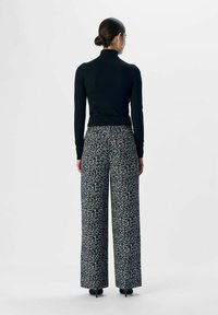 Zwarte neklijn met opstaand boord, gecombineerd met wijde broek in een grijs panterprint. Het materiaal lijkt zacht met een gladde textuur.