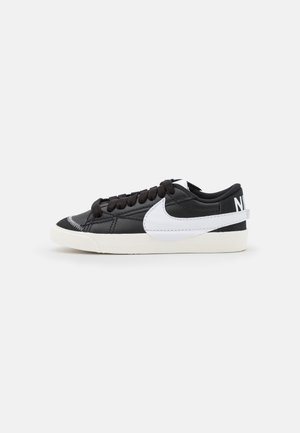 Czarny niski sneaker Nike z białym logo swoosh i podeszwa, czarnymi sznurówkami oraz napisem "NIKE" na pasku przy pięcie.