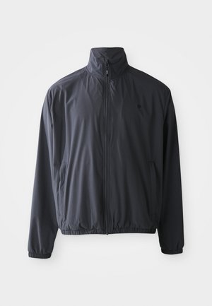 Melnā vieglā jaka ar pilnu priekšējo rāvējslēdzēju, stāvošu apkakli, elastīgām aprocēm un sānu kabatām uz vienkrāsaina balta fona.