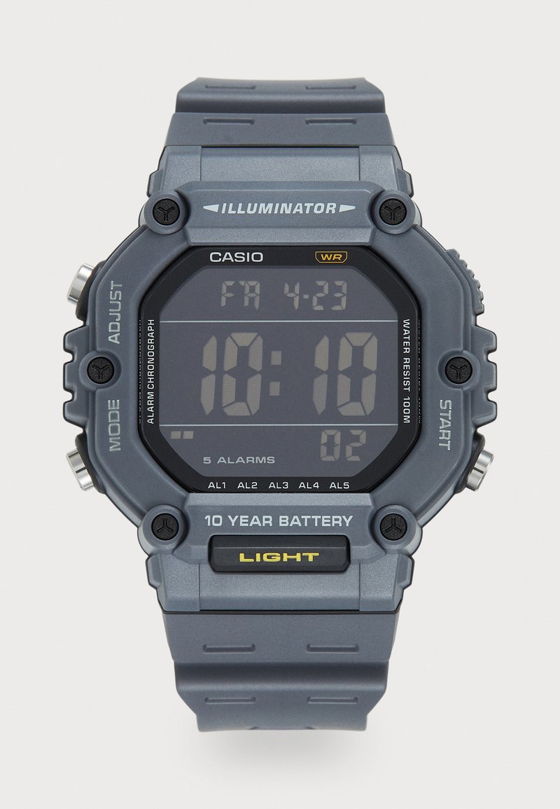 Montre numérique avec un écran rectangulaire noir et un bracelet en caoutchouc gris. Les caractéristiques incluent une résistance à l'eau, des fonctions d'alarme et une autonomie de 10 ans.