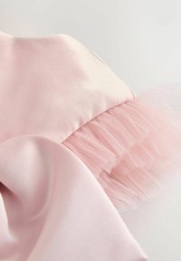 Hellrosa Stoff mit einer glatten Satin-Oberfläche, versehen mit einem gerafften Tüllakzent am Saum für zusätzlichen Textur und Detail.