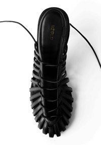 Sandal in pelle nera con design aperto sulla punta e cinturini incrociati. Presenta una superficie liscia e una suola piatta. Nome del brand impresso all'interno.