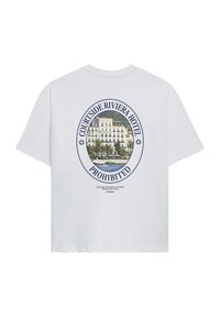 Λευκό T-shirt με οβάλ γραφικό ενός ξενοδοχείου στο νερό, φοίνικες και το κείμενο «Courtside Riviera Hotel Prohibited» στην πλάτη.