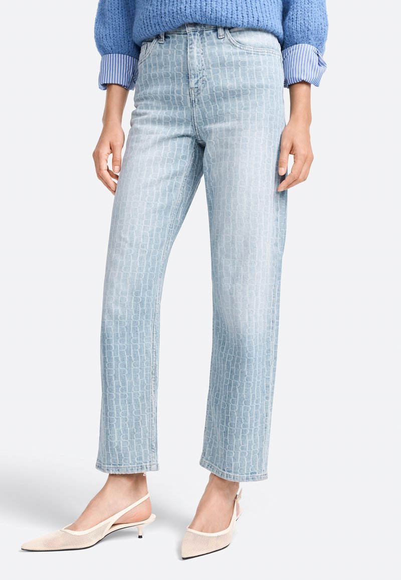 Jeans azzurri chiari con una trama a motivo, vita alta e gamba dritta. Abbinati a scarpe beige con tacco a rocchetto e punta affusolata.