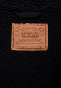 Juodas tekstūruotas medžiagos ženkliukas su iškiliosiomis raidėmis. Etiketėje užrašyta "BIG STAR" su "TAVO GYVENIMAS. TAVO DŽINSAI" po ja. Nurodyta vidutinė dydis.