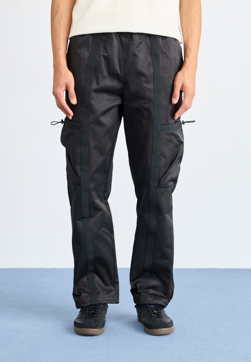 Calças cargo pretas com uma textura suave, apresentando dois bolsos laterais, cordões ajustáveis e riscas laterais em preto contrastante.