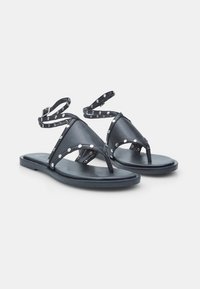 Zwarte leren sandalen met een teenslipperontwerp, studaccenten en verstelbare enkelriemen op een platte zool.