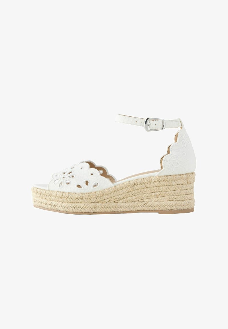 Sandale compensée blanche avec plateforme en jute tressé, bride à la cheville avec boucle, et motifs floraux découpés sur les bords festonnés.