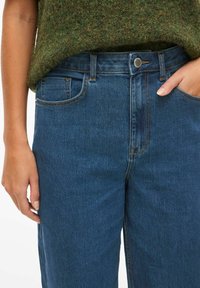 Jeans de mezclilla azules con cintura alta, bolsillos frontales y costuras en contraste. La tela presenta un lavado azul clásico y una textura suave.