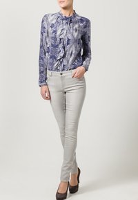 Blus med lång ärm i blå och vit print med volangdetalj vid kragen, matchad med ljusgrå slim-fit byxor och mörka klackar.