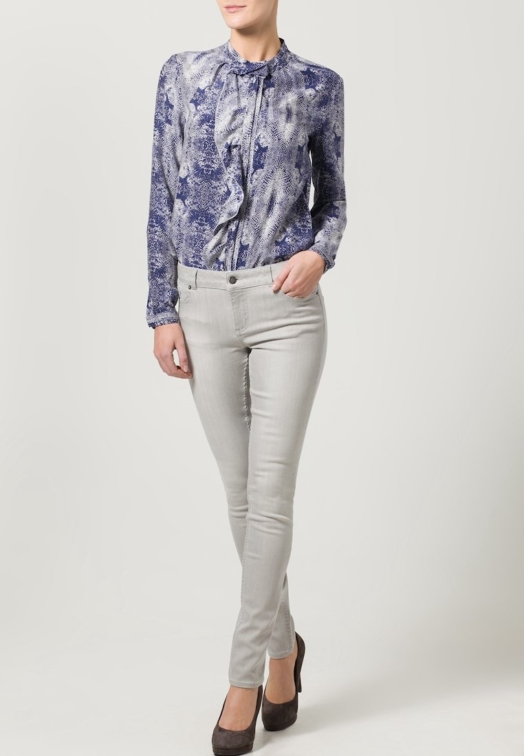 Blus med lång ärm i blå och vit print med volangdetalj vid kragen, matchad med ljusgrå slim-fit byxor och mörka klackar.