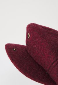 Burgundy felt cap featuring a rounded shape, button closure, and a soft texture. Inside is lined with a smooth fabric, enhancing comfort.
