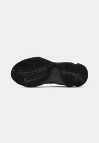 Semelle de chaussure noire avec motif de grip texturé et logo Nike Swoosh, vue de dessous sur un fond clair uni.