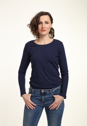 Marineblauwe longsleeve jersey top met een ronde halslijn, gecombineerd met lichtblauwe jeans. De stof lijkt zacht met een gladde textuur.