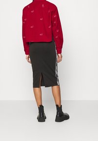 Red cropped shirt with white logo graphics paired with a black knee-length skirt featuring side stripes and a back split, worn with black boots.