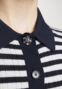 Polo a righe navy e bianche in maglia con una spilla in cristallo al colletto e un bottone nero e bianco con il marchio "MAX&Co."