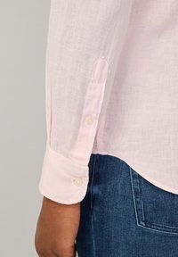 Camicia di lino rosa chiaro con polsini bottonati, caratterizzata da una leggera texture, orlo curvo e jeans in denim blu a contrasto.
