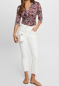 Blouse à motif floral avec un col en V profond et des manches bouffantes, associée à un jean en denim blanc taille haute et des sandales dorées à lanières. Sac à main blanc.