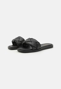 Sandali neri a scivolo realizzati in pelle sintetica testurizzata con un design a fascia incrociata e suola piatta e liscia. Stile leggero e minimalista.