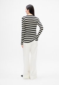 Top de manga larga a rayas en blanco y negro combinado con pantalones anchos y blancos; textura suave y diseño ajustado con un escote redondeado.