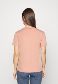 T-shirt z krótkim rękawem, okrągłym dekoltem, uszyty z miękkiej brzoskwiniowej bawełny. Charakteryzuje się prostym wzorem, gładką strukturą, prostym dołem oraz luźnym krojem.