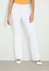 Jean blanc évasé à taille haute au design minimaliste. Fabriqué en tissu denim, avec des poches avant et une fermeture par bouton.