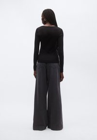 Musta pitkähihaisen yläosa yhdistetty harmaisiin leveälahkeisiin farkkuihin. Rakenteellinen neuloskangas sileällä viimeistelyllä; näkyvät saumat ja taskut.