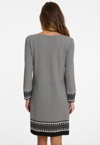 Schwarz-weißer kariierter Kleid mit langen Ärmeln, das einen gemusterten Saum und die Ärmelbündchen aufweist. Glatte Stofftextur.