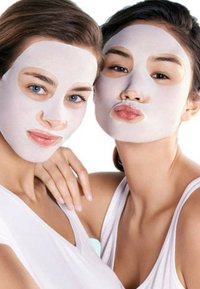 Due persone che indossano maschere bianche con ritagli per gli occhi e la bocca, entrambe in top bianchi senza maniche, in una posa ravvicinata, sorridenti.