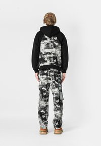 Sudadera negra con un patrón abstracto texturizado en gris y blanco en la parte posterior; combinada con pantalones a juego que presentan un diseño similar y etiquetas laterales.