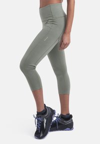 Grønne, midt-læg leggings lavet af glat stof med gule syninger og et højt talje-bånd, parret med sorte sportsko med lilla accenter.