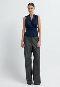 Blusa senza maniche blu navy con bottoni e vita arricciata, abbinata a pantaloni grigi a vita alta e gamba larga con glitter e leggere spezie argentate.