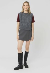 Pull sans manches en maille grise avec un motif texturé, associé à une mini-jupe grise et des bottes en cuir noir jusqu'aux genoux.