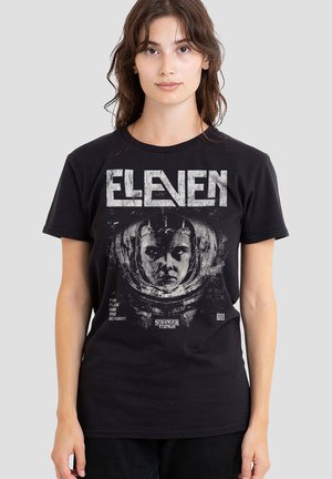 Black cotton t-shirt featuring a graphic of a character in an astronaut helmet, with the text "ELEVEN" and "STRANGER THINGS" in bold print.