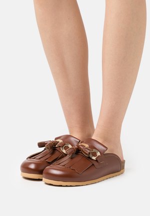 Sabots en cuir marron avec une finition lisse, ornés de franges et de nœuds décoratifs. Semelle en caoutchouc beige durable. Design à dos ouvert.