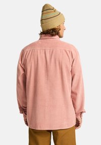 Rosa kordflorte skjorta med långa ärmar, bakparti och knappärmar. Bärs med en beige stickad mössa med flerfärgade ränder.