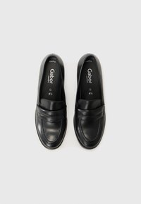 Black leather loafers with a wide strap and stitch detailing. Features a rounded toe and low profile, designed for comfort.