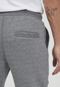 Grå teksturerte joggebukser med baklomme med klaff, laget av et elastisk stoff for komfort.