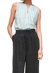 Blusa senza maniche a righe blu chiaro e bianco con scollatura a V e due tasche frontali, abbinata a pantaloni neri larghi con coulisse.
