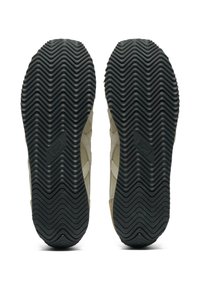 Svart gummisula med zigzag-mönster. Beige ovandel med texturerade paneler. Har präglad logotypdetalj nära hälen.