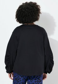 Camisa de manga larga negra con mangas fruncidas, hecha de una tela suave. Escote redondeado, corte relajado y sutiles costuras en la parte posterior.