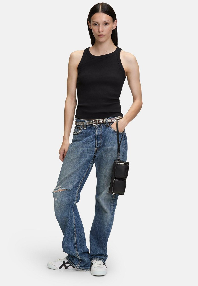 Top negro de canalé, jeans azules desgastados, cinturón plateado con tachuelas, pequeño bolso cruzado negro y zapatillas blancas con detalles en negro.